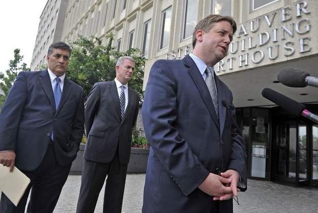 3 men in suits outside a building with one man talking to the microphone