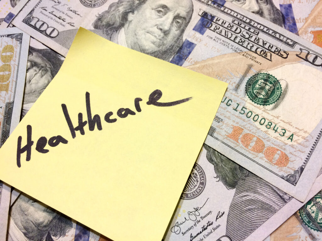 "Healthcare" written on a sticky note on top of several hundred dollar bills. Healthcare fraud concept.