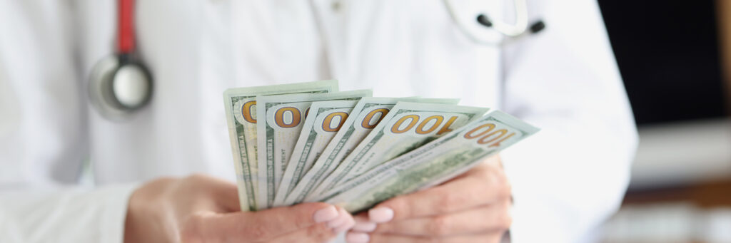 Doctor holding hundred dollar bills. Healthcare fraud concept.