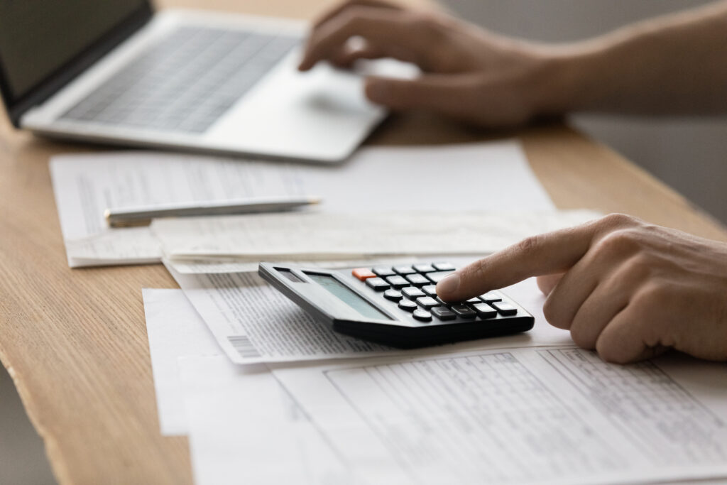 A person working at a desk with a calculator and documents preparing to submit fraudulent billing information. Healthcare fraud concept.
