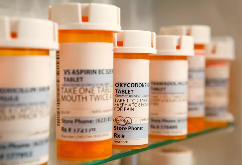A row of prescription medications in orange pill bottles sitting on a shelf in a pharmacy. Healthcare fraud concept.
